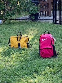 two backpacks sitting on the grass in front of a fence